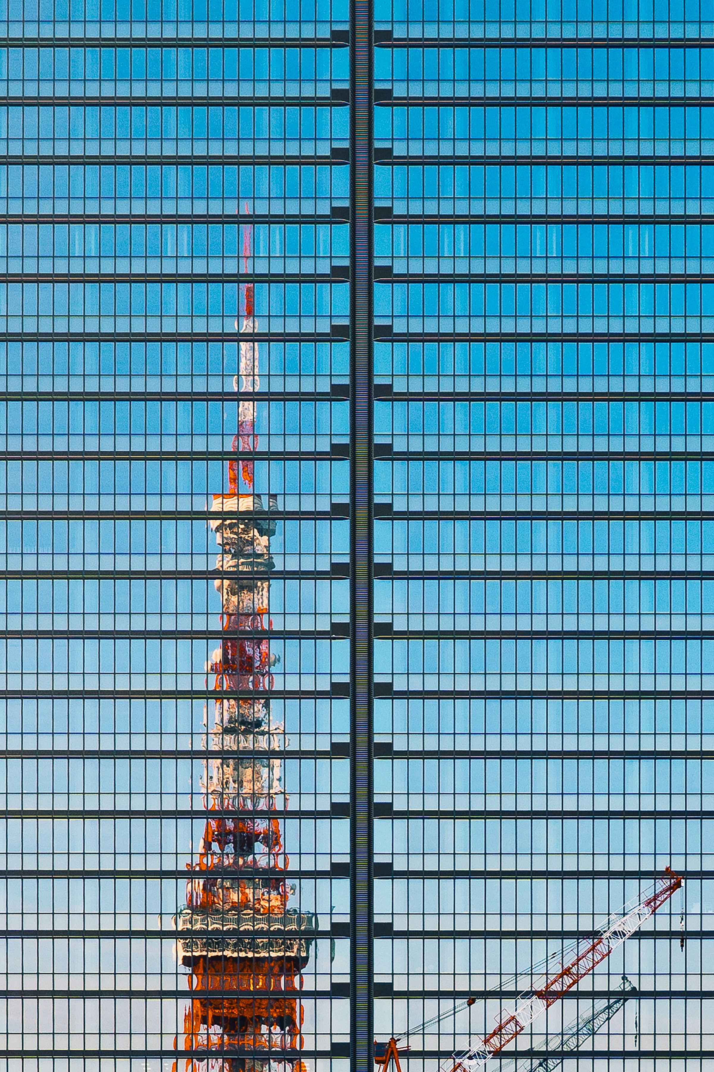 Tokyo Tower reflected in the glass facade of a skyscraper against a blue evening sky.